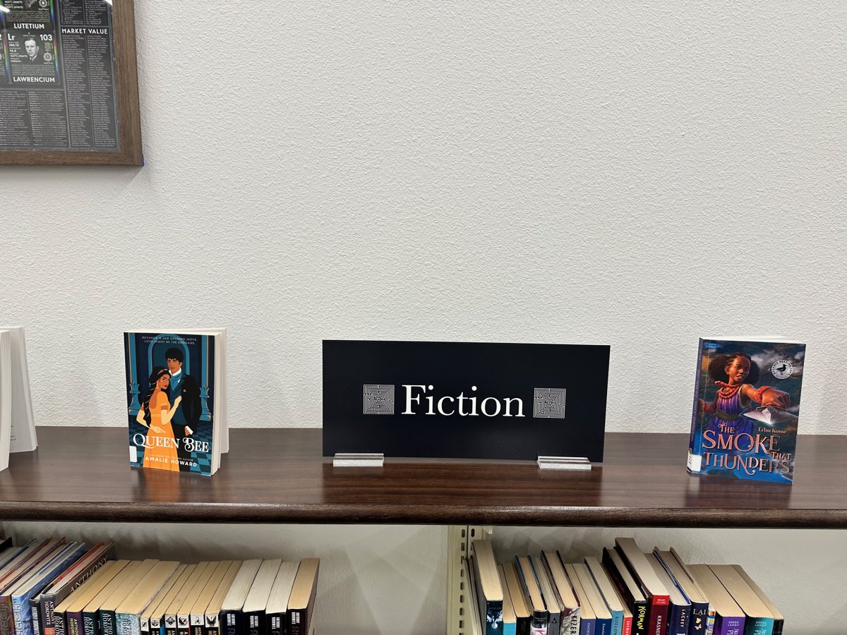 The fiction sign on the walnut shelf top, the framed periodic table in the corner above.