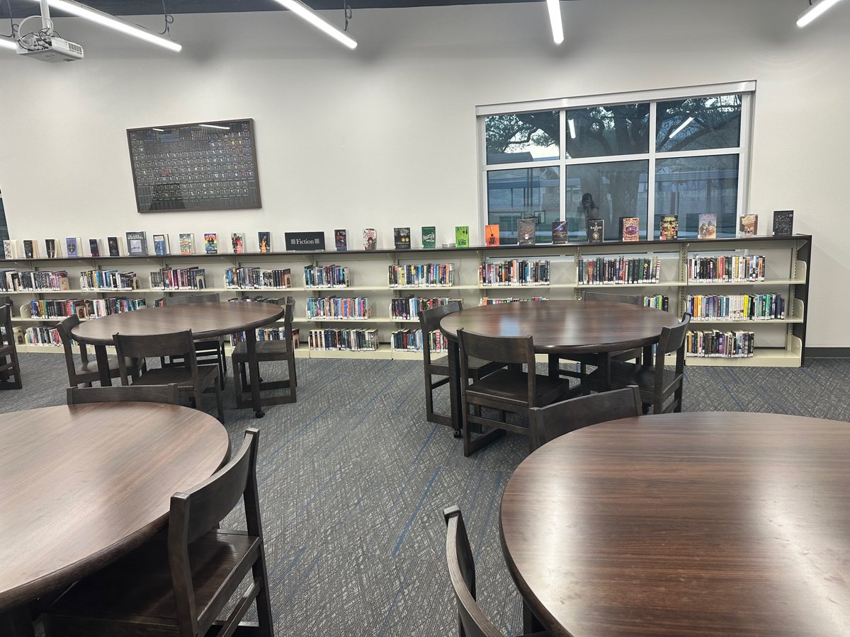 After: walnut round tables and chairs, the fiction wall behind them, the framed periodic table on the wall.