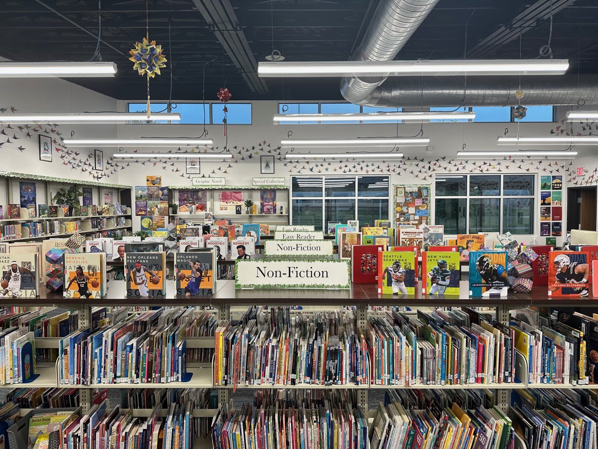 Non-Fiction and Easy Reader signage above the shelves, cranes crossing the wall behind.